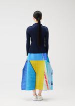 A woman with long dark hair in a ponytail faces away, wearing PLEATS PLEASE ISSEY MIYAKE's CITY COLLAGE navy top and pleated skirt featuring blue, yellow, and red townscape patterns, paired with white sneakers against a plain background.