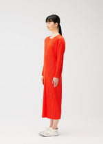 A woman with straight black hair in a ponytail stands sideways, wearing a bright orange PLEATS PLEASE ISSEY MIYAKE MONTHLY COLORS : FEBRUARY long-sleeved, round-neck dress and white sneakers against a plain white background.