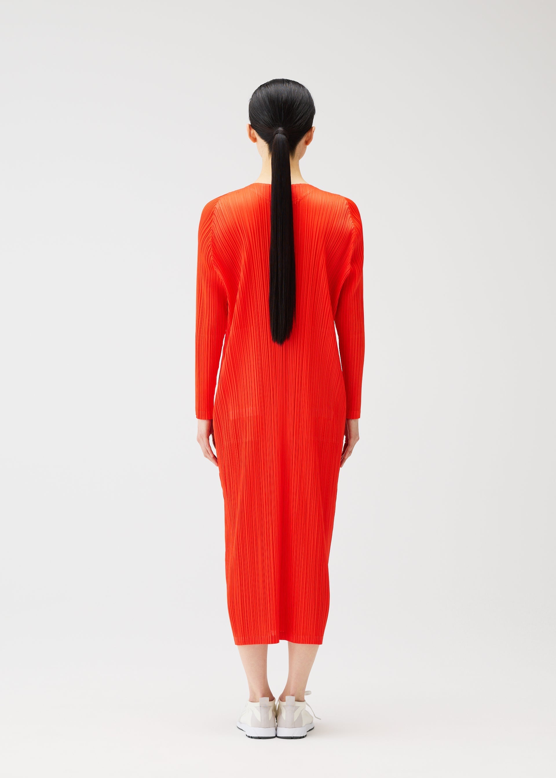 Zoomed view A person with long black hair in a ponytail, seen from behind, wears a bright red PLEATS PLEASE ISSEY MIYAKE MONTHLY COLORS : FEBRUARY long-sleeved dress and white sneakers against a plain white background.