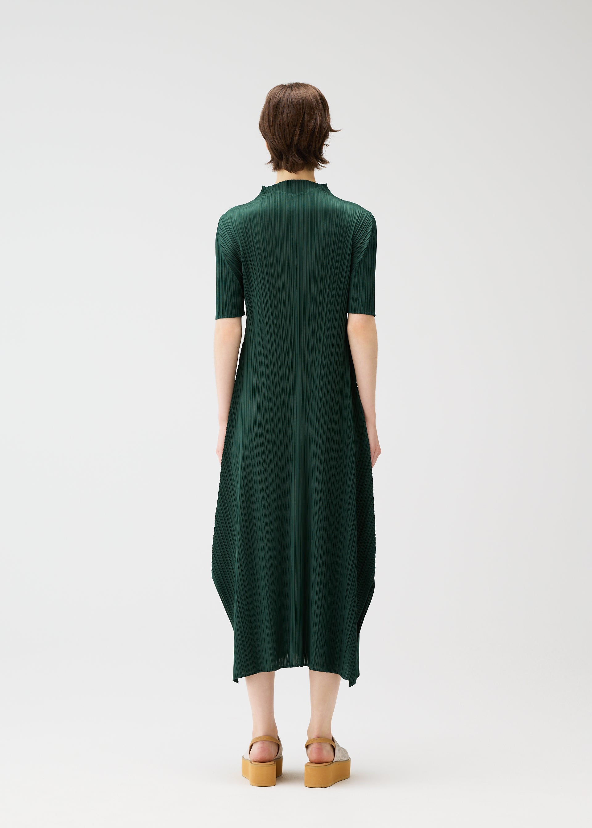 Zoomed view A person with short brown hair faces away, wearing the MONTHLY COLORS : MARCH mid-length dress by PLEATS PLEASE ISSEY MIYAKE and tan platform sandals against a plain white background.