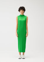 A person with short curly hair wears the MONTHLY COLORS : APRIL high-neck sleeveless dress by PLEATS PLEASE ISSEY MIYAKE in light green with vertical pleats, paired with white sneakers, standing against a plain white background.