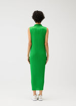 A person with short curly hair wears the MONTHLY COLORS : APRIL high-neck sleeveless bright green pleated dress by PLEATS PLEASE ISSEY MIYAKE and white sneakers, standing against a plain white background.