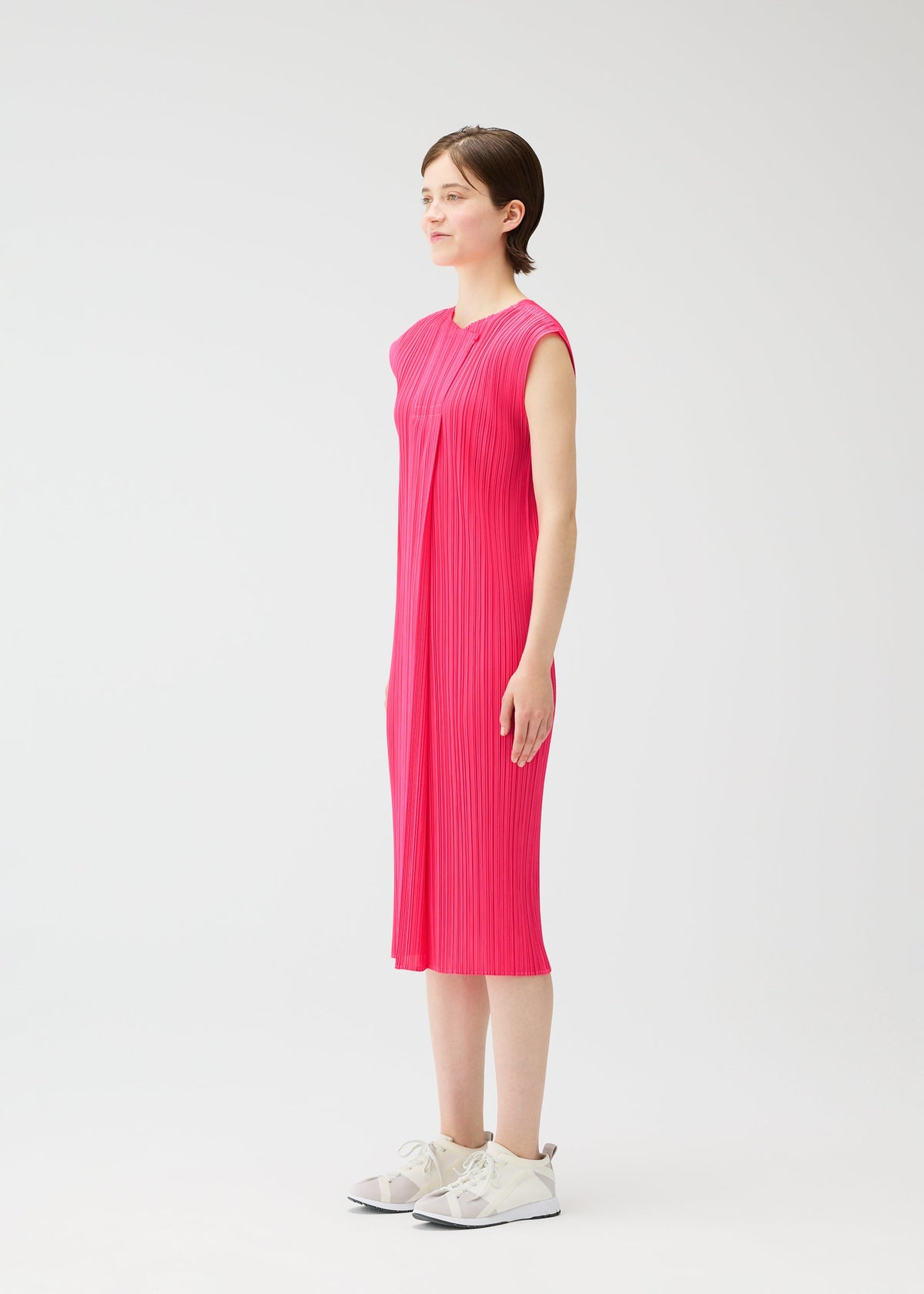 A person stands in profile wearing the knee-length, sleeveless MONTHLY COLORS : JUNE dress by PLEATS PLEASE ISSEY MIYAKE with white sneakers, set against a plain white background. view 8 of 10
