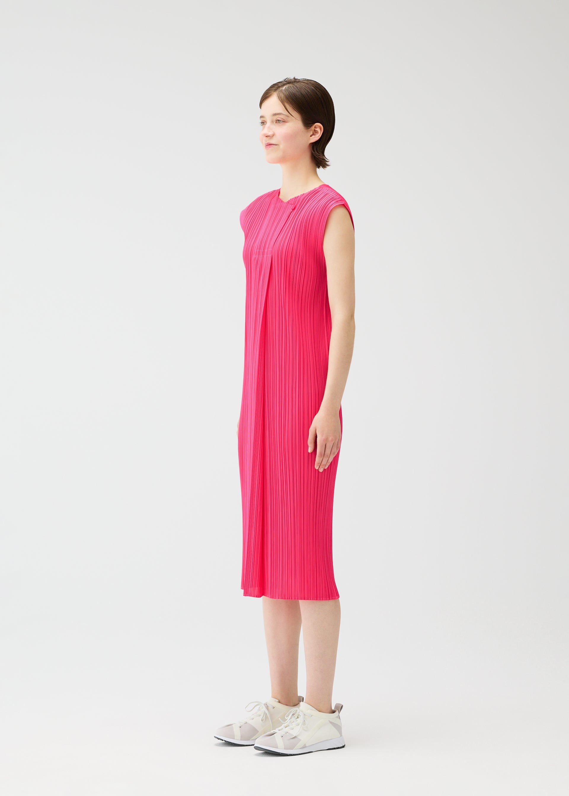 Zoomed view A person stands in profile wearing the knee-length, sleeveless MONTHLY COLORS : JUNE dress by PLEATS PLEASE ISSEY MIYAKE with white sneakers, set against a plain white background.
