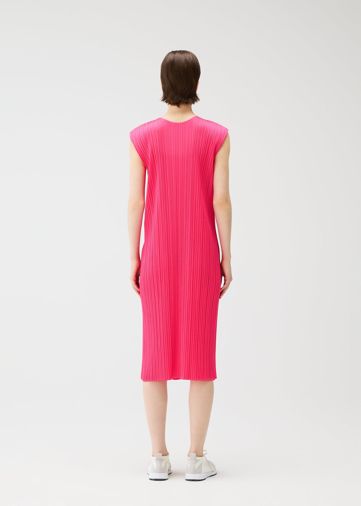 A person stands facing away, wearing the bright pink MONTHLY COLORS : JUNE sleeveless knee-length pleated dress by PLEATS PLEASE ISSEY MIYAKE, paired with white sneakers against a plain white background. view 9 of 10
