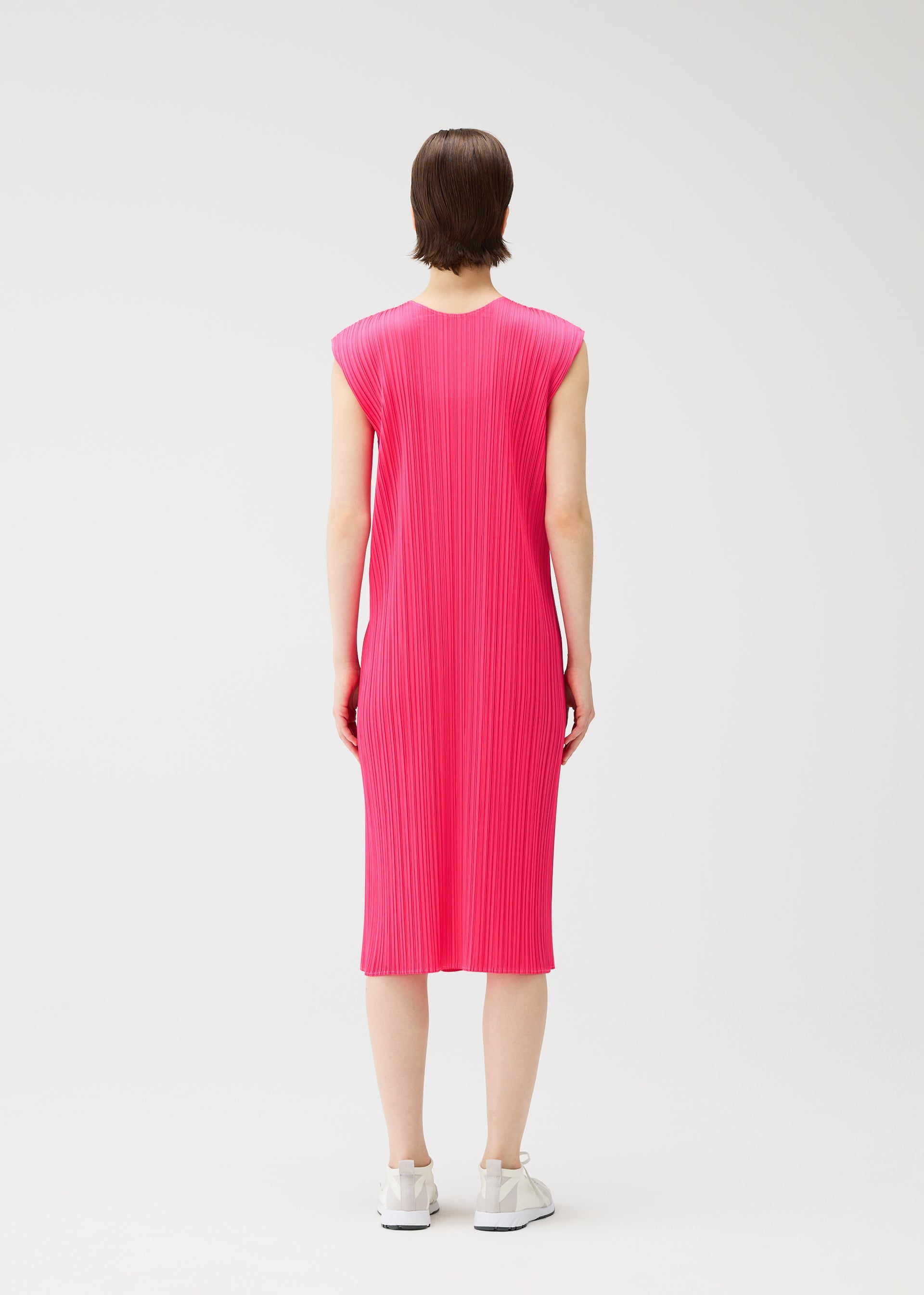 Zoomed view A person stands facing away, wearing the bright pink MONTHLY COLORS : JUNE sleeveless knee-length pleated dress by PLEATS PLEASE ISSEY MIYAKE, paired with white sneakers against a plain white background.
