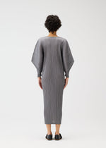 A person with short, curly hair is seen from behind wearing the SKYLINE long gray pleated round-neck dress with dolman sleeves by PLEATS PLEASE ISSEY MIYAKE and black slip-on shoes against a plain white background.