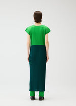 A person with short brown hair, seen from behind, wears the SWING dress by PLEATS PLEASE ISSEY MIYAKE in bright green and dark teal with cap sleeves, paired with matching dark teal pants and black shoes against a plain light background.