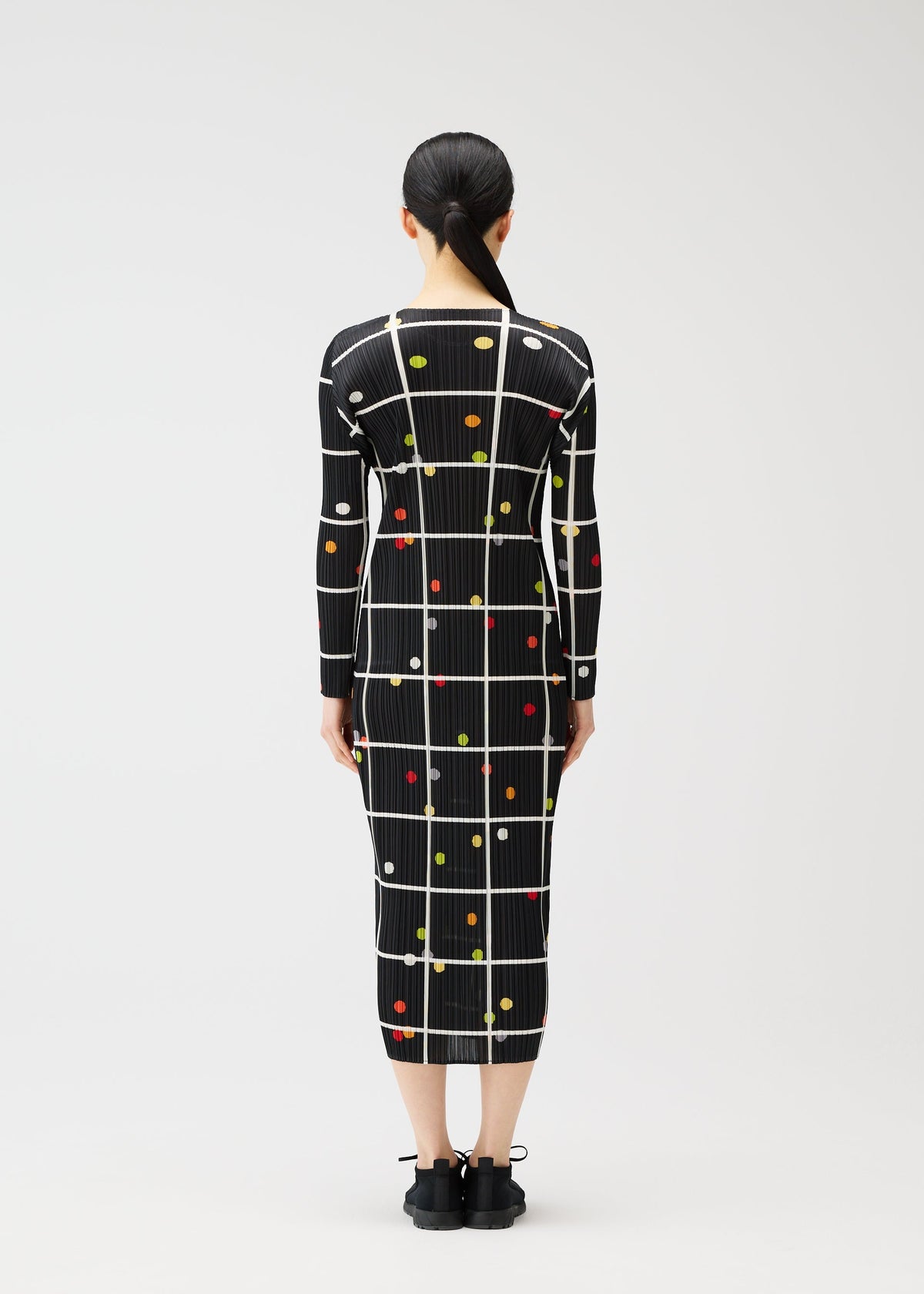 A person faces away, wearing the CROSSING DOTS dress by PLEATS PLEASE ISSEY MIYAKE—a printed, long-sleeved, round-neck style featuring white grid lines and colorful dots. The fitted silhouette is paired with hair tied back in a low ponytail. view 6 of 7