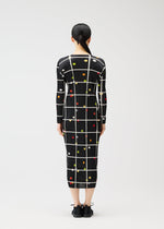 A person faces away, wearing the CROSSING DOTS dress by PLEATS PLEASE ISSEY MIYAKE—a printed, long-sleeved, round-neck style featuring white grid lines and colorful dots. The fitted silhouette is paired with hair tied back in a low ponytail.