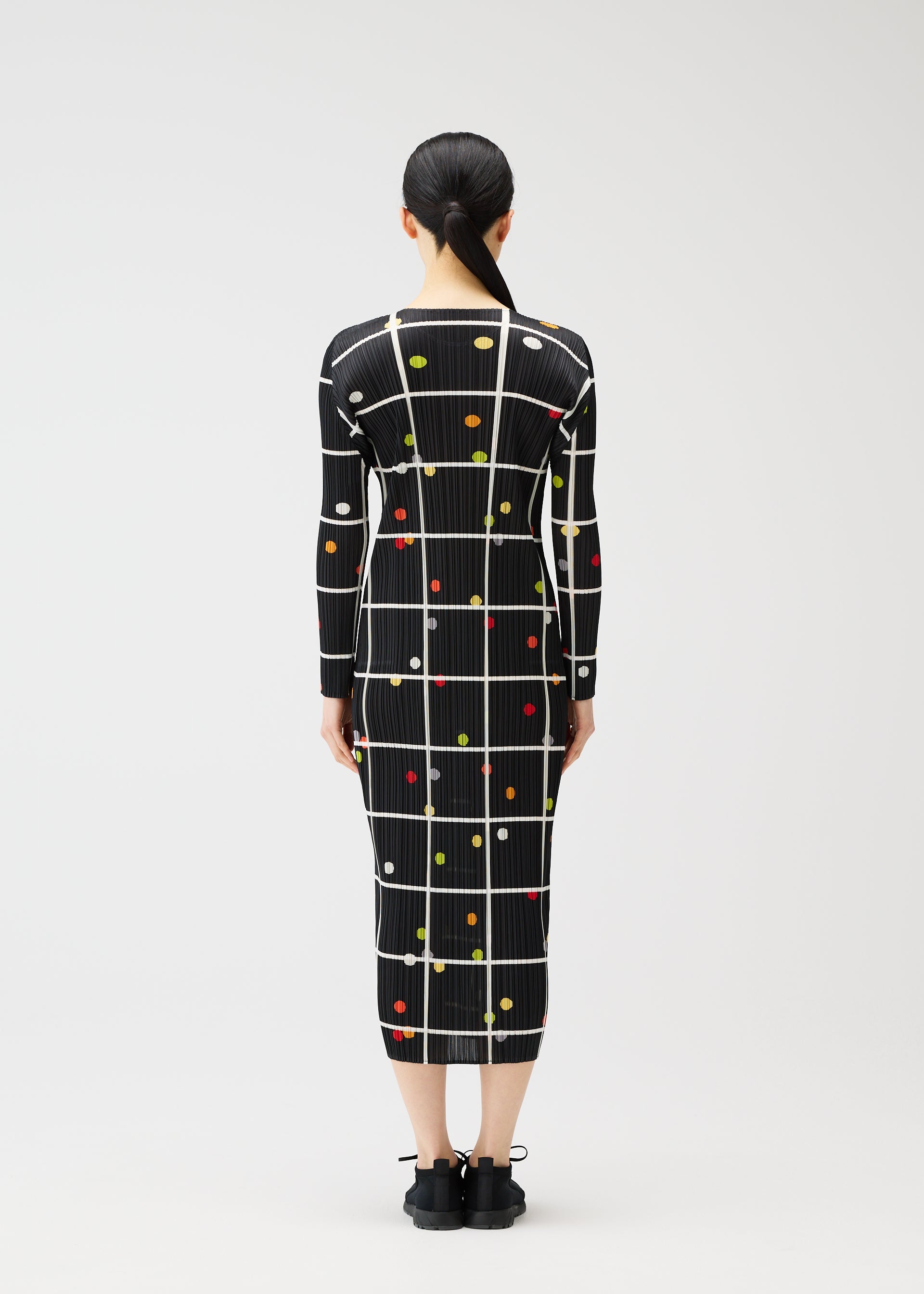 Zoomed view A person faces away, wearing the CROSSING DOTS dress by PLEATS PLEASE ISSEY MIYAKE—a printed, long-sleeved, round-neck style featuring white grid lines and colorful dots. The fitted silhouette is paired with hair tied back in a low ponytail.