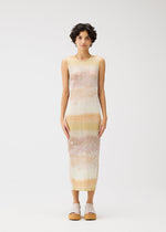 A person with short curly hair wears the SEA BUBBLE sleeveless, ankle-length pleated dress in pastel tie-dye by PLEATS PLEASE ISSEY MIYAKE, paired with light platform sandals against a plain white background.