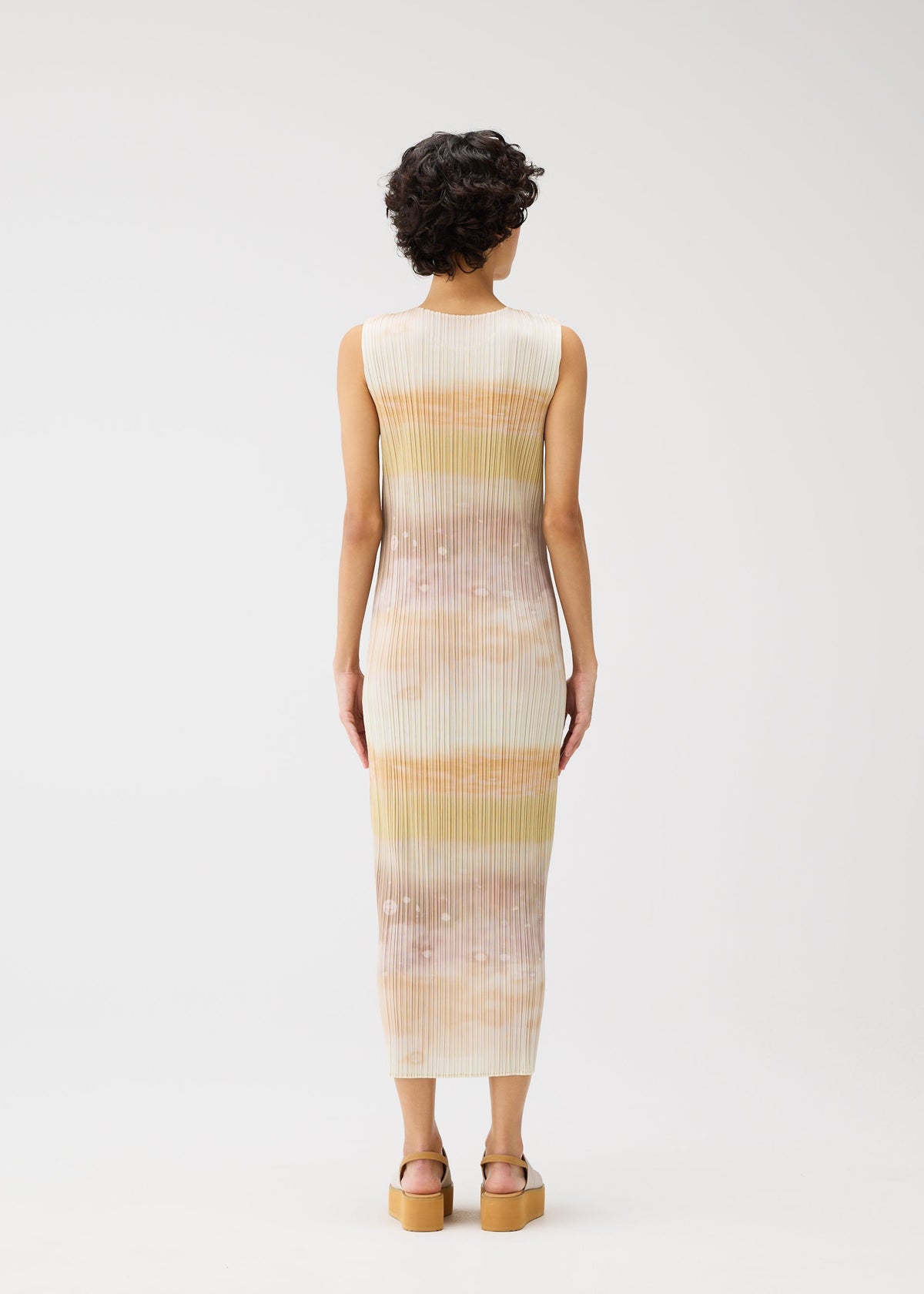 A person with short curly hair faces away, wearing the ankle-length ribbed SEA BUBBLE dress by PLEATS PLEASE ISSEY MIYAKE—sleeveless with horizontal pastel stripes and platform sandals—set against a plain white background. view 6 of 6