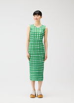 A woman with straight dark hair and bangs stands against a white background, wearing the PLEATS PLEASE ISSEY MIYAKE BASKET sleeveless calf-length green block check print dress and beige platform sandals. She has a neutral expression.