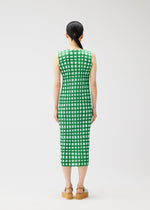 A woman with straight black hair in a low ponytail stands facing away, wearing the PLEATS PLEASE ISSEY MIYAKE BASKET green and white block check sleeveless midi dress and tan platform sandals against a plain white background.
