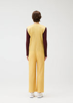 A person with short brown hair faces away, wearing the PLEATS PLEASE ISSEY MIYAKE THICKER BOTTOMS 1 yellow zippered jumpsuit over a long-sleeve burgundy top and white sneakers, set against a plain light background.