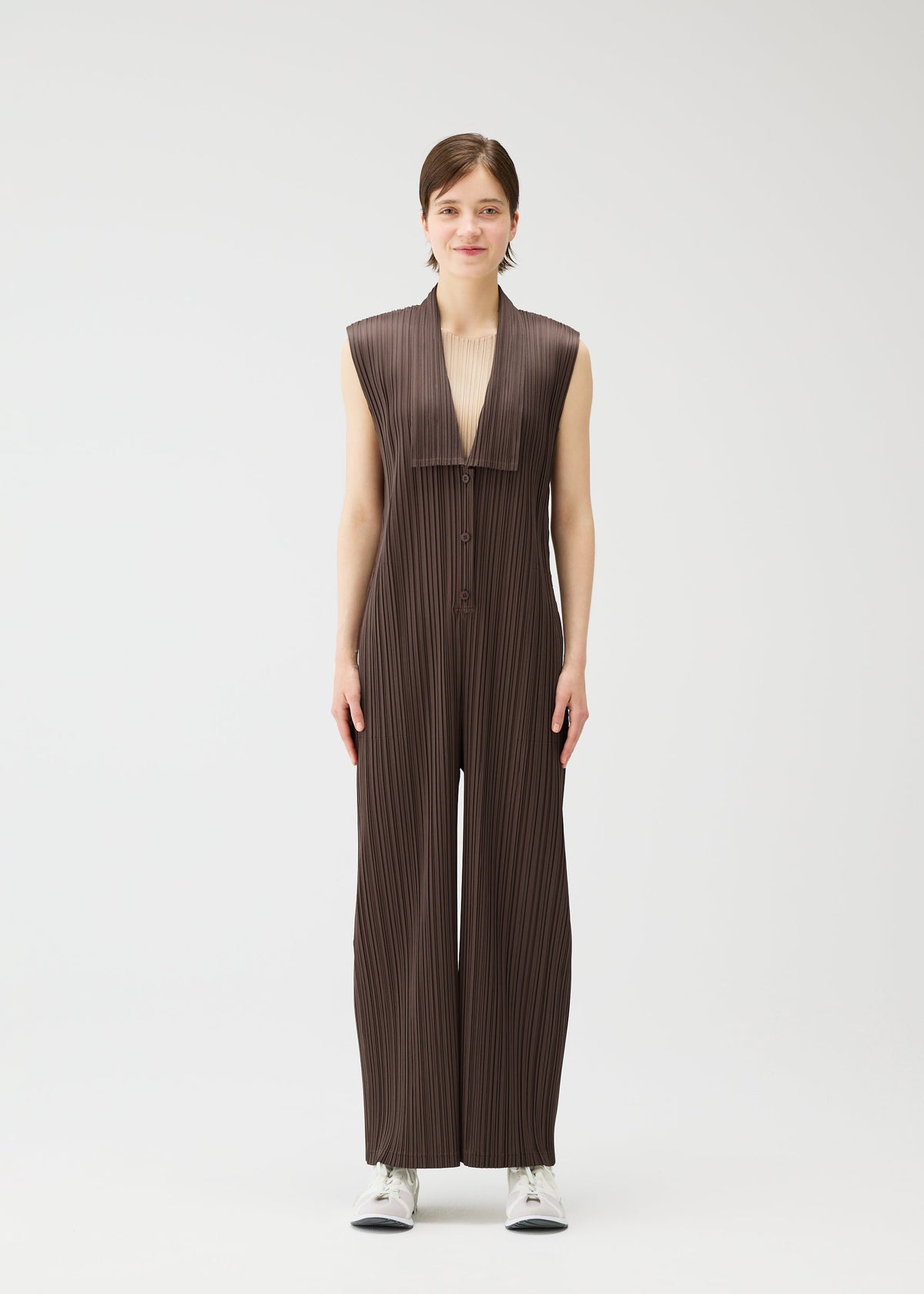 A woman faces forward wearing PLEATS PLEASE ISSEY MIYAKE LOOP BOTTOMS, sleeveless and pleated with wide legs, crafted from recycled polyester with button closures, paired with white sneakers against a plain background. view 5 of 8