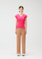 A woman with short brown hair and a neutral expression wears the MONTHLY COLORS : JUNE bright pink pleated top and beige wide-legged pleated pants from PLEATS PLEASE ISSEY MIYAKE, styled with white sneakers against a plain white background.