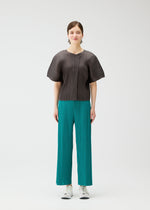 A person stands against a white background wearing items from PLEATS PLEASE ISSEY MIYAKE's MONTHLY COLORS : JUNE collection, including a pleated top and teal pleated wide-leg pants, styled with white sneakers and drop earrings.