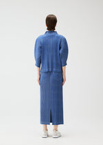 A person with short brown hair wears the PLEATS PLEASE ISSEY MIYAKE COTTON DENIM ribbed long-sleeve top and matching calf-length skirt, paired with white sneakers. They stand against a plain white background, facing away.