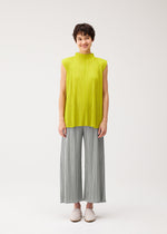 A person with short dark hair smiles, wearing PLEATS PLEASE ISSEY MIYAKE's MELLOW PLEATS bright yellow-green sleeveless top and light gray pleated wide-leg pants, with slip-on shoes, standing against a white background.