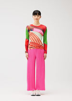 A person with short dark hair stands against a white background wearing the CITY COLLAGE long-sleeved top with abstract patterns and pink wide-leg pleated pants by PLEATS PLEASE ISSEY MIYAKE, paired with white sneakers.