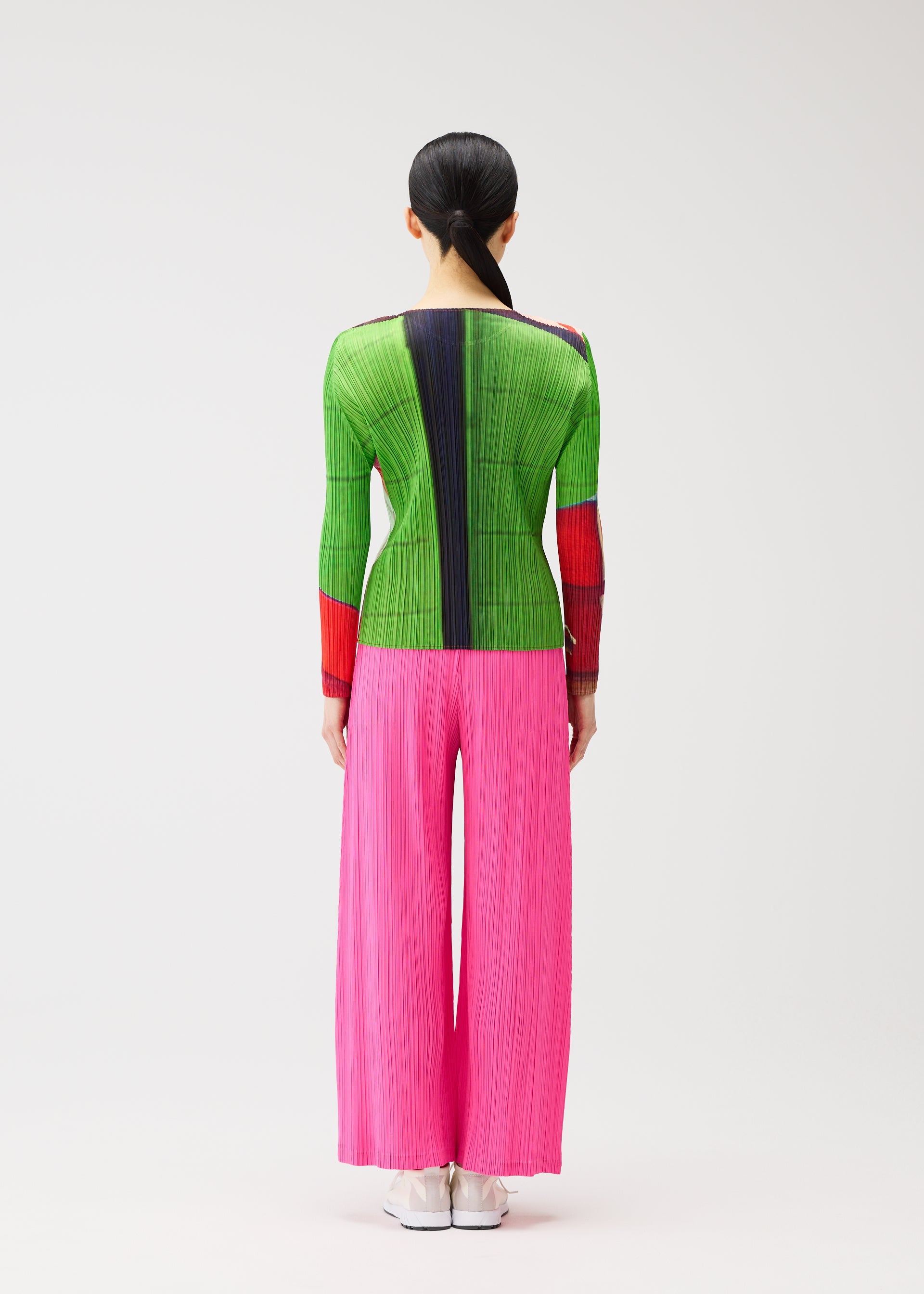 Zoomed view A person with long black hair in a low ponytail wears the CITY COLLAGE top and bright pink pleated pants by PLEATS PLEASE ISSEY MIYAKE, standing facing away against a plain background.
