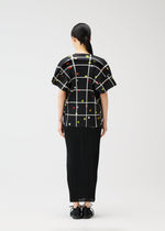 A person with dark hair in a low ponytail faces away, wearing the black textured "CROSSING DOTS" top by PLEATS PLEASE ISSEY MIYAKE with a grid and colorful dots, paired with black shoes, against a plain white background.