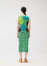 A person with long dark hair in a ponytail models the MARKET dress by PLEATS PLEASE ISSEY MIYAKE—a sleeveless, calf-length green and white checkered dress with blue, green, and brown circular patterns—paired with tan platform sandals.