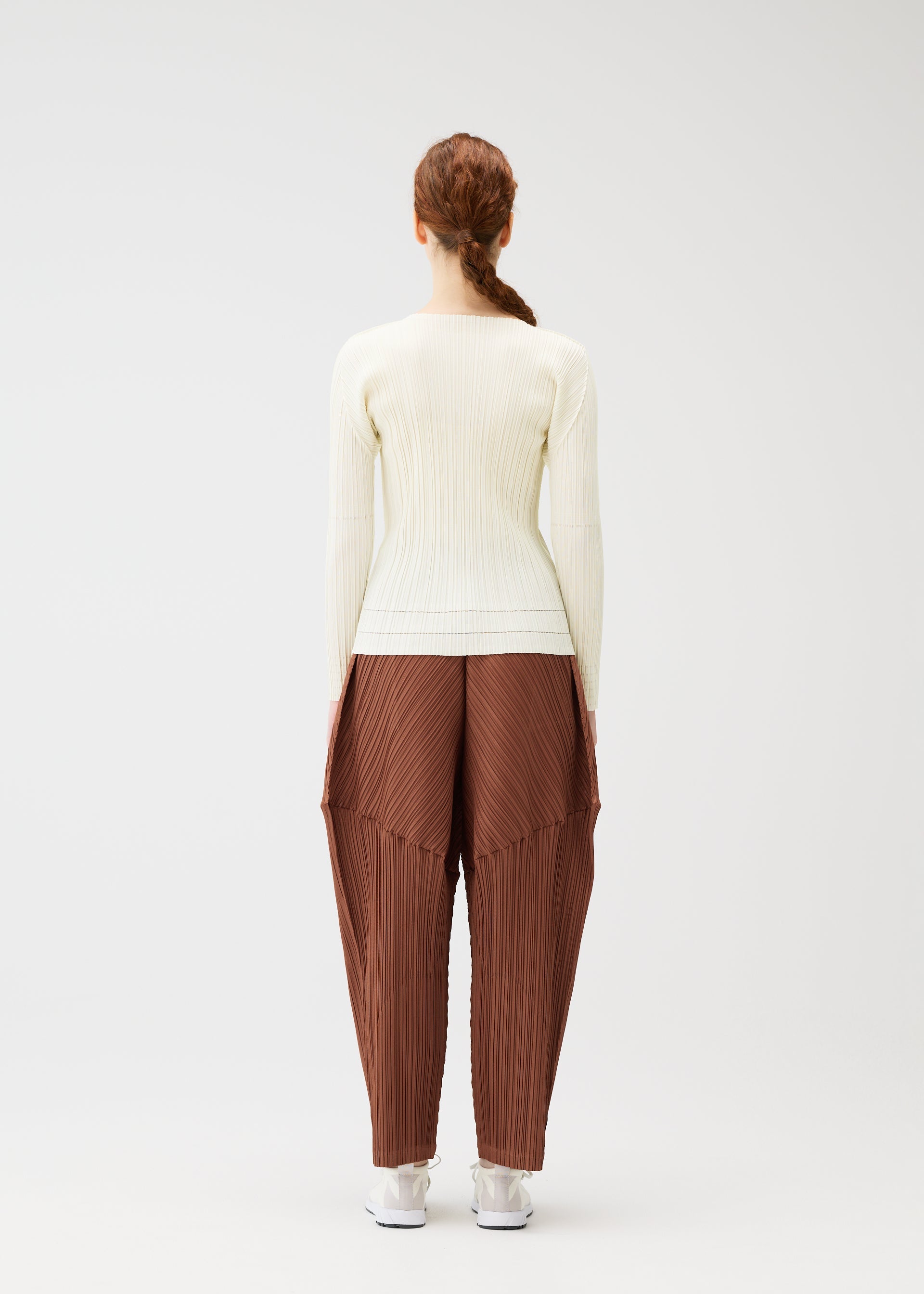Zoomed view A person with long, auburn braided hair wears the SOFT PLEATS cream top and brown pleated pants by PLEATS PLEASE ISSEY MIYAKE, standing with their back to a plain white background.