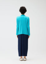 A person with short curly hair, seen from behind, wears the PLEATS PLEASE ISSEY MIYAKE MONTHLY COLORS: JANUARY collection—a bright turquoise cardigan and long navy pleated skirt—paired with white flats against a plain white background.
