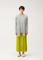 A person stands facing forward, dressed in MELLOW PLEATS by PLEATS PLEASE ISSEY MIYAKE: a light gray pleated long-sleeve top, soft-textured matching cardigan, and bright yellow-green pleated wide-leg pants. They wear light beige shoes against a plain background.