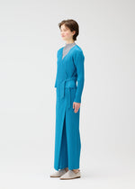 A person stands sideways against a white background, wearing the bright blue FACADE pleated wrap jacket and matching wide-leg pants by PLEATS PLEASE ISSEY MIYAKE, paired with a light gray high-neck top and light-colored shoes.
