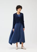 A person wears the CITY FRAME navy pleated dress and matching cardigan by PLEATS PLEASE ISSEY MIYAKE, paired with light slip-on shoes, standing against a plain white background.