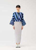 A woman with straight dark hair and a slight smile models the CITY COLLAGE set by PLEATS PLEASE ISSEY MIYAKE: a blue striped wide-sleeved top, long light gray pleated skirt, and white sneakers against a plain white background.