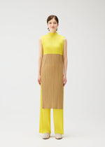 A woman with short brown hair models the SWING high-neck sleeveless tunic by PLEATS PLEASE ISSEY MIYAKE, featuring pleated yellow fabric and a contrasting brown front panel, shown against a minimal white studio backdrop.