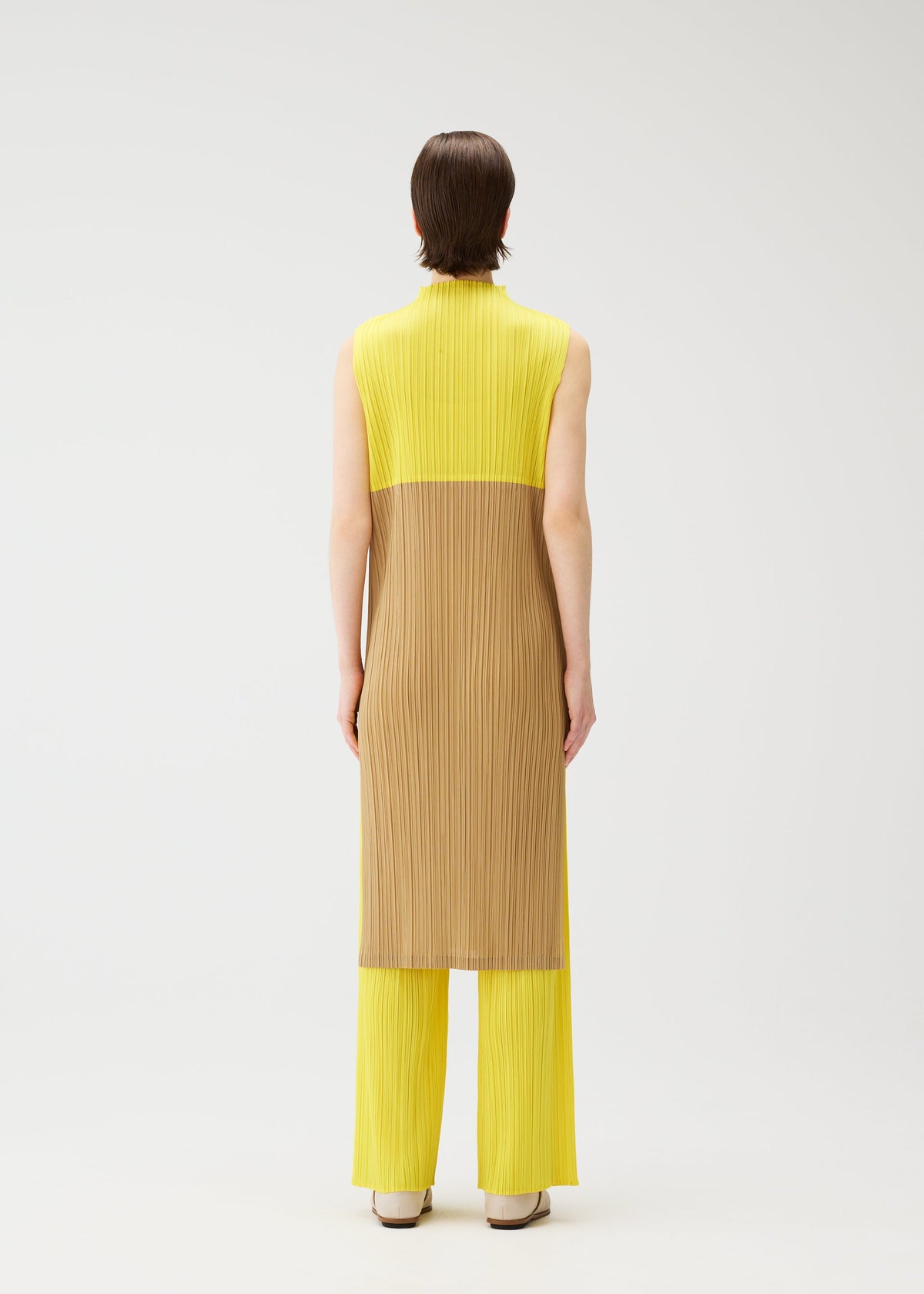 A person faces away, wearing the SWING high-neck sleeveless tunic with a yellow and brown pleated design, paired with matching yellow pleated pants from PLEATS PLEASE ISSEY MIYAKE. The background is plain white. view 9 of 12