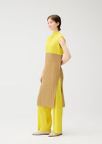 A person stands against a plain white background, wearing the SWING high-neck sleeveless tunic and matching yellow pleated pants by PLEATS PLEASE ISSEY MIYAKE, styled with beige shoes for a versatile look.