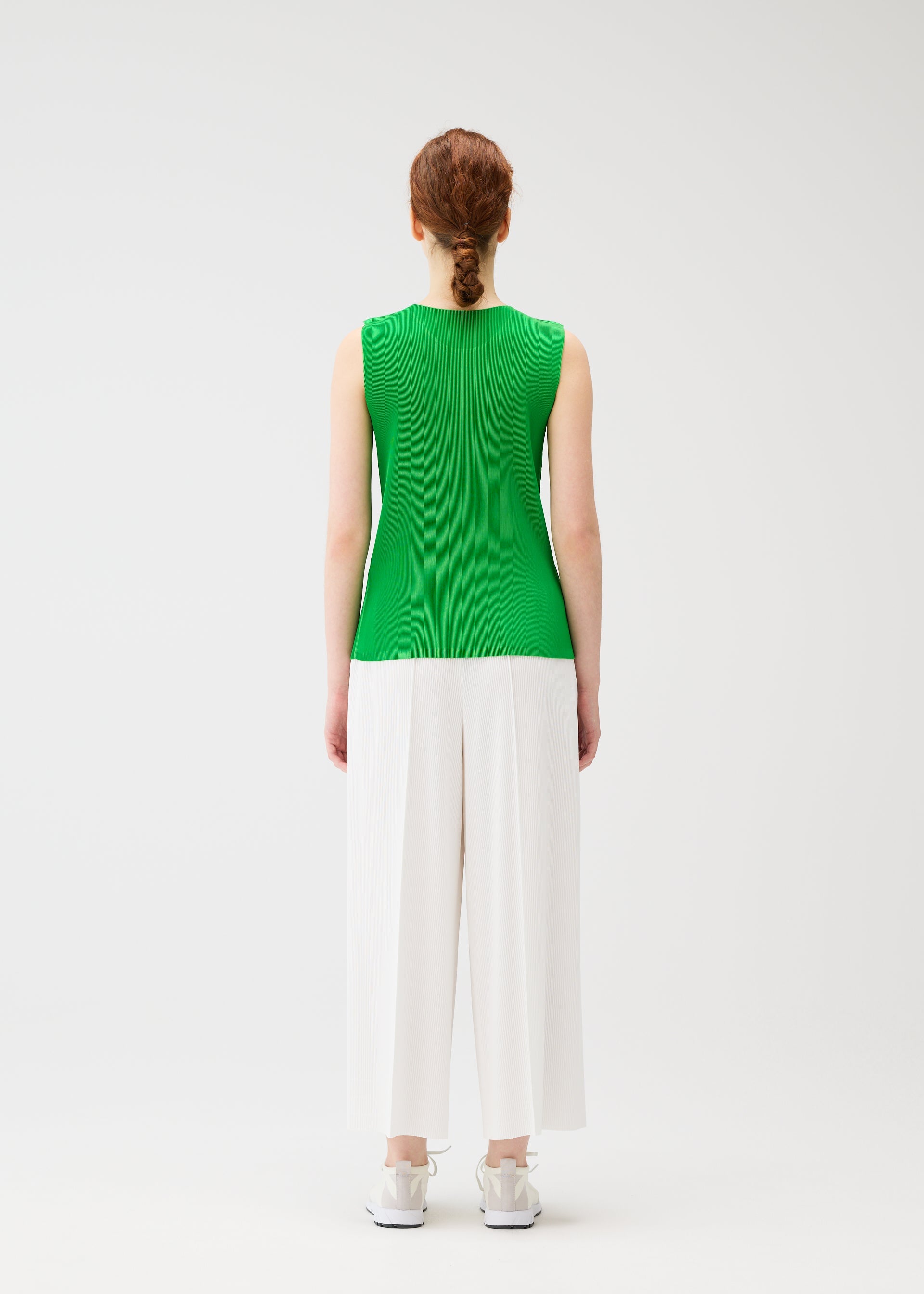 Zoomed view A woman with red hair in a braid wears PLEATS PLEASE ISSEY MIYAKE A-POC BOTTOMS and a sleeveless green top, standing facing away against a plain white background.
