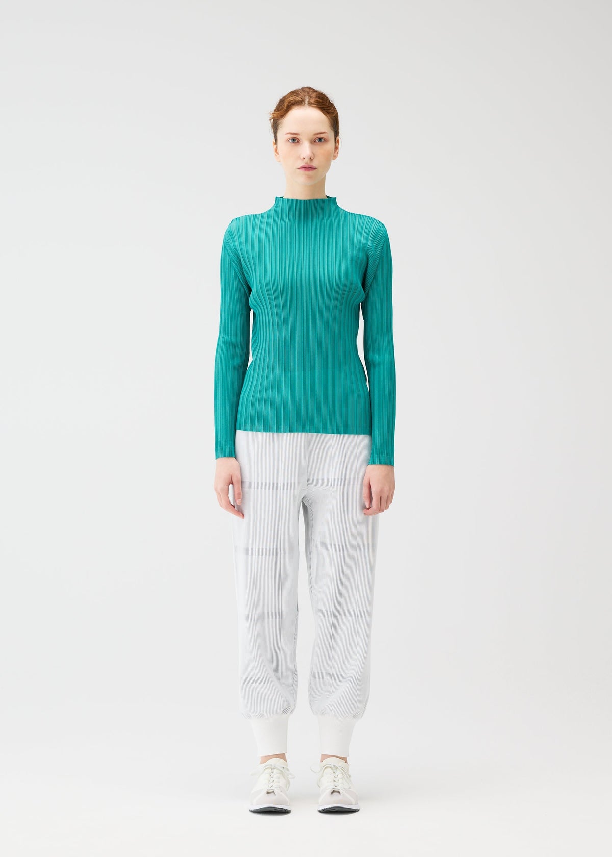 A woman faces forward against a white background, wearing the CROSSING KNIT teal ribbed sweater from PLEATS PLEASE ISSEY MIYAKE, paired with light gray plaid pants and white sneakers. view 4 of 7