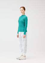 A woman with light skin and auburn hair tied back stands sideways against a plain white background, wearing the PLEATS PLEASE ISSEY MIYAKE CROSSING KNIT in teal, paired with white plaid pants and white sneakers.