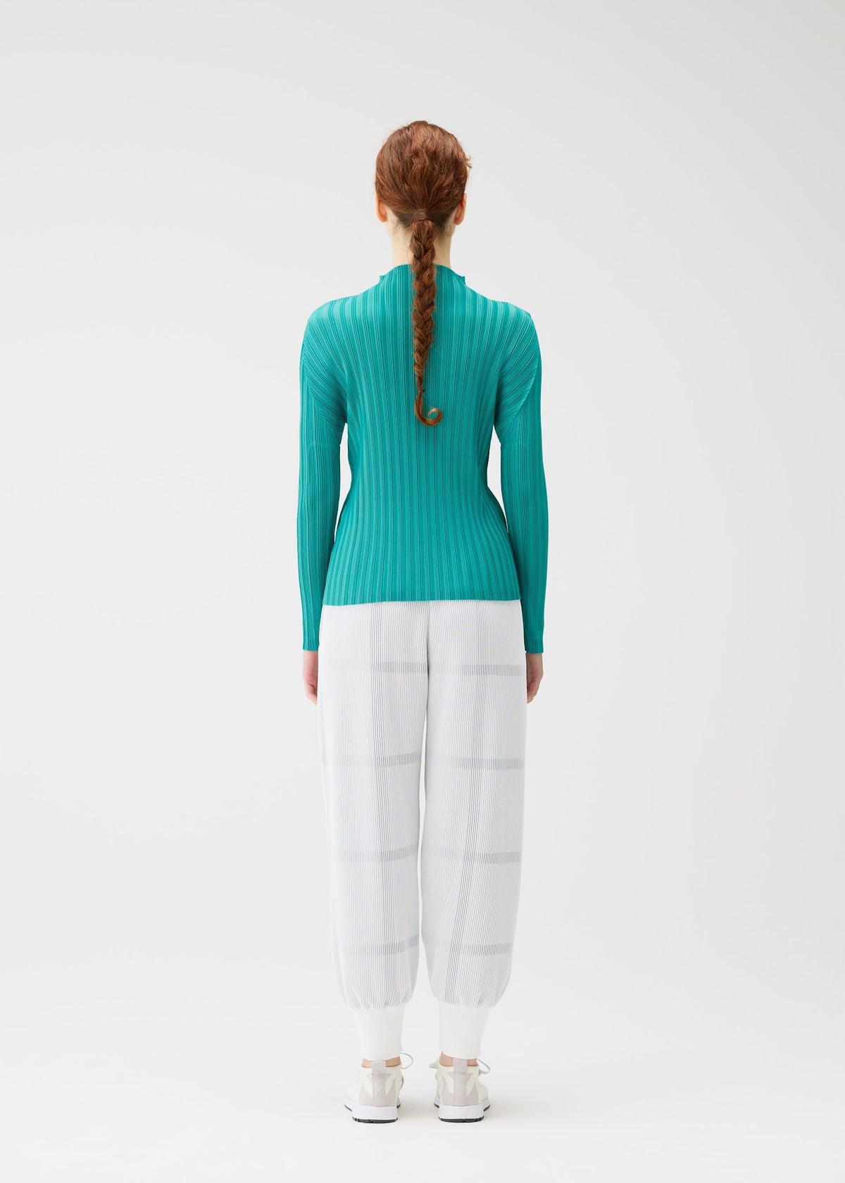 A woman with long, braided red hair faces away, wearing the CROSSING KNIT top by PLEATS PLEASE ISSEY MIYAKE, paired with sheer white wide-leg pants and white shoes against a plain white background. view 6 of 7
