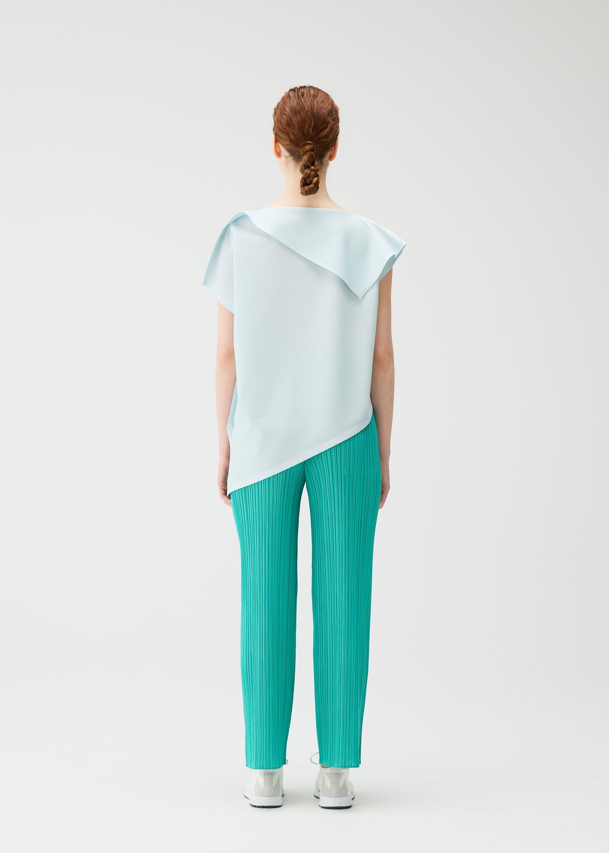 A person with red hair in a low bun faces away, wearing PLEATS PLEASE ISSEY MIYAKE's A-POC SEA GLASS top and teal pleated pants, paired with white sneakers, all set against a plain white background. view 8 of 8