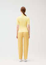 A person with long red hair in a braid stands facing away, wearing the yellow RIB KNIT set from PLEATS PLEASE ISSEY MIYAKE and white shoes, against a plain white background.