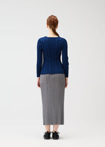 A person with long red hair in a braid faces away, wearing a fitted blue RIB KNIT top and gray pleated skirt by PLEATS PLEASE ISSEY MIYAKE, with black shoes, against a plain light background.