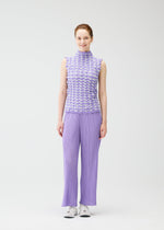 A woman faces forward, smiling, wearing the PLEATS PLEASE ISSEY MIYAKE TWIST KNIT sleeveless lavender top and wide-leg pants with white sneakers against a plain white background.