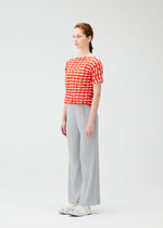 A woman with light skin and brown hair tied back stands sideways against a white background, wearing the PLEATS PLEASE ISSEY MIYAKE TWIST KNIT top, light gray pleated wide-leg pants, and white sneakers.