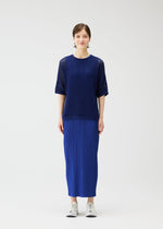 A person stands facing forward wearing the PLEATS PLEASE ISSEY MIYAKE FISHNET KNIT top and matching pleated skirt with white sneakers, against a plain white background.
