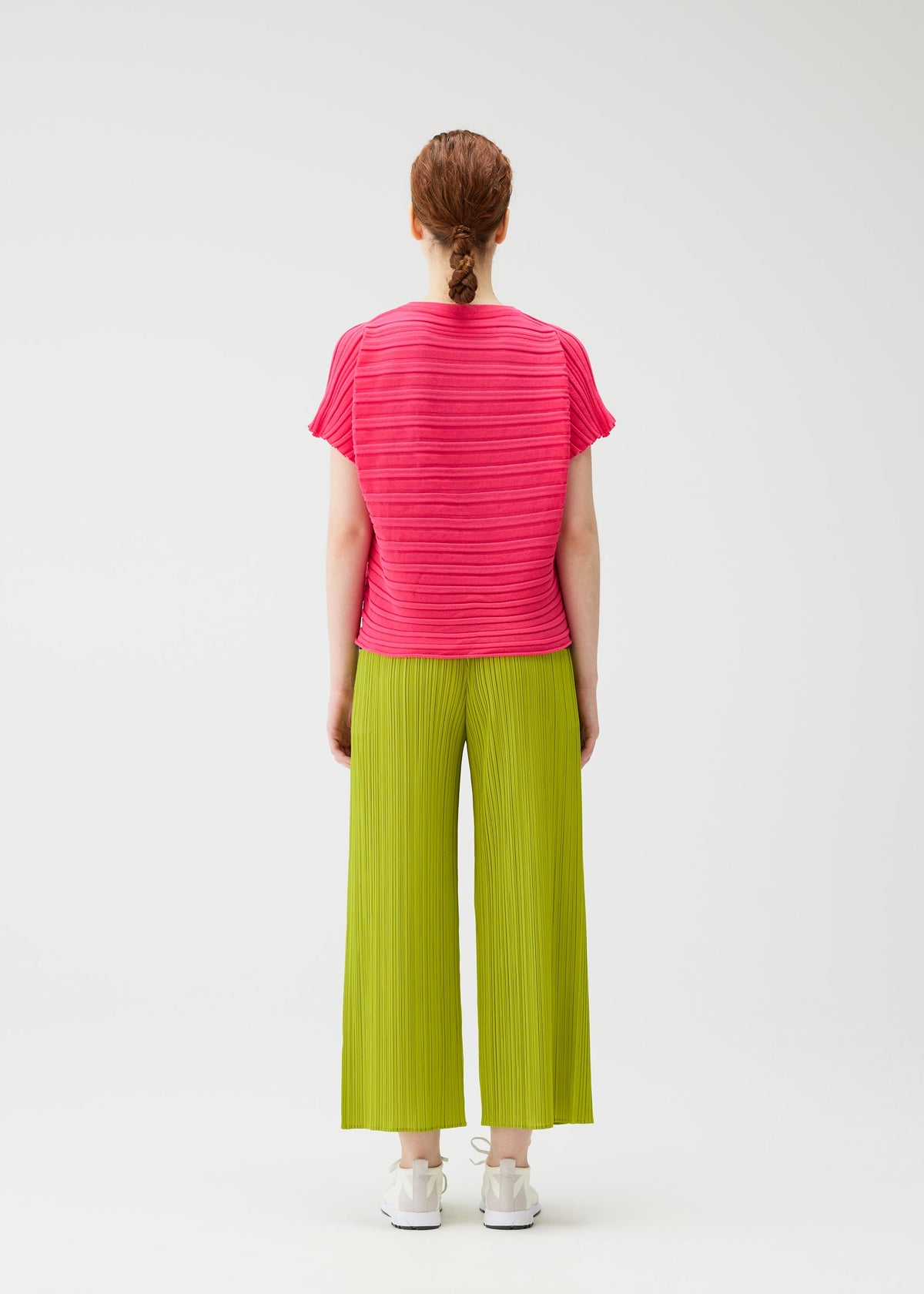 A person stands facing away, wearing the STEP KNIT short-sleeve top and wide-legged pleated pants by PLEATS PLEASE ISSEY MIYAKE, paired with white sneakers. Their hair is tied back against a plain white background—ideal for summer looks. view 7 of 7