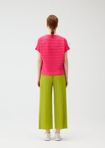 A person stands facing away, wearing the STEP KNIT short-sleeve top and wide-legged pleated pants by PLEATS PLEASE ISSEY MIYAKE, paired with white sneakers. Their hair is tied back against a plain white background—ideal for summer looks.